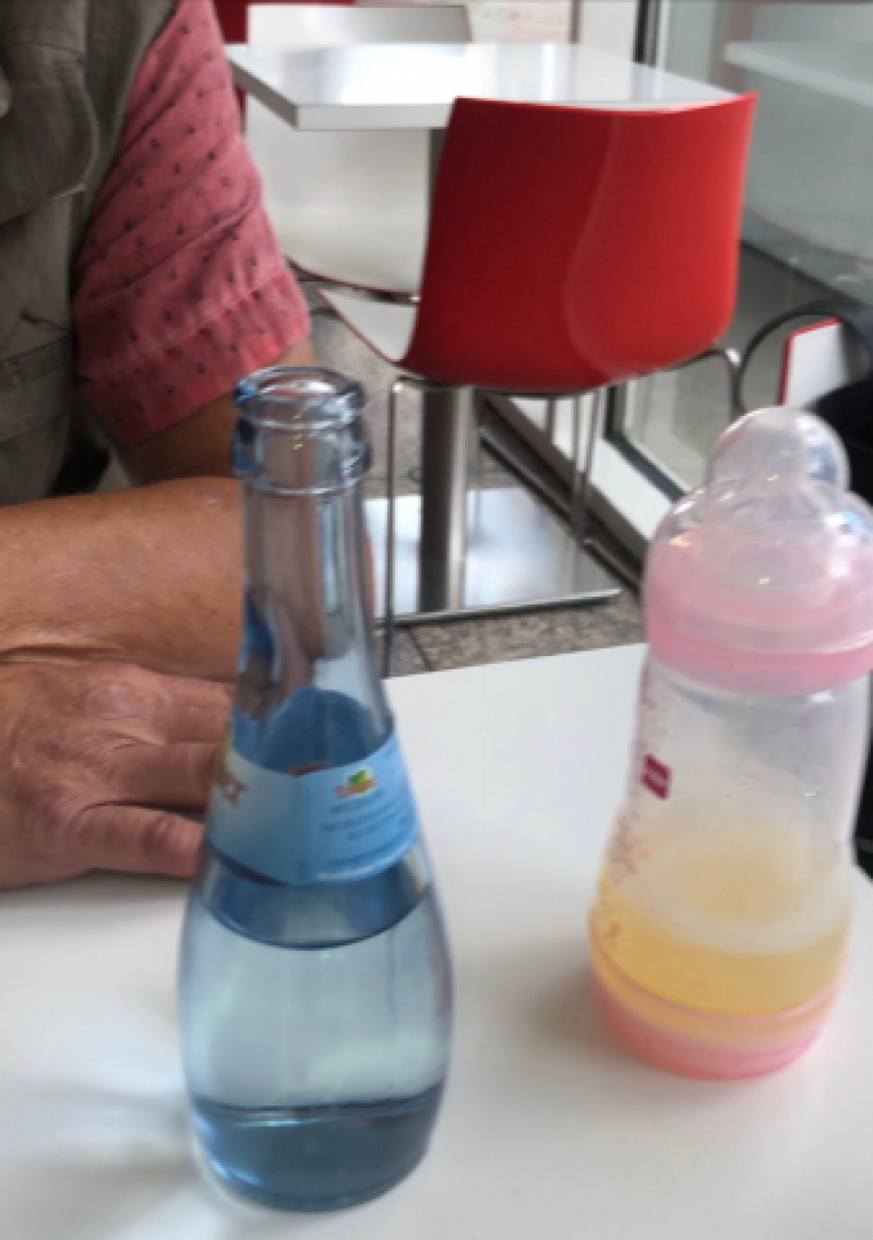 Public - Adult Baby trinkt Natursekt aus dem Fläschchen